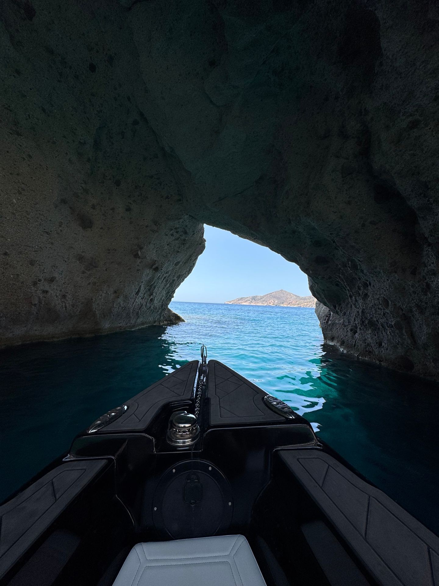 Entering a rocky sea cave on a boat with view of clear blue ocean and distant coastline.