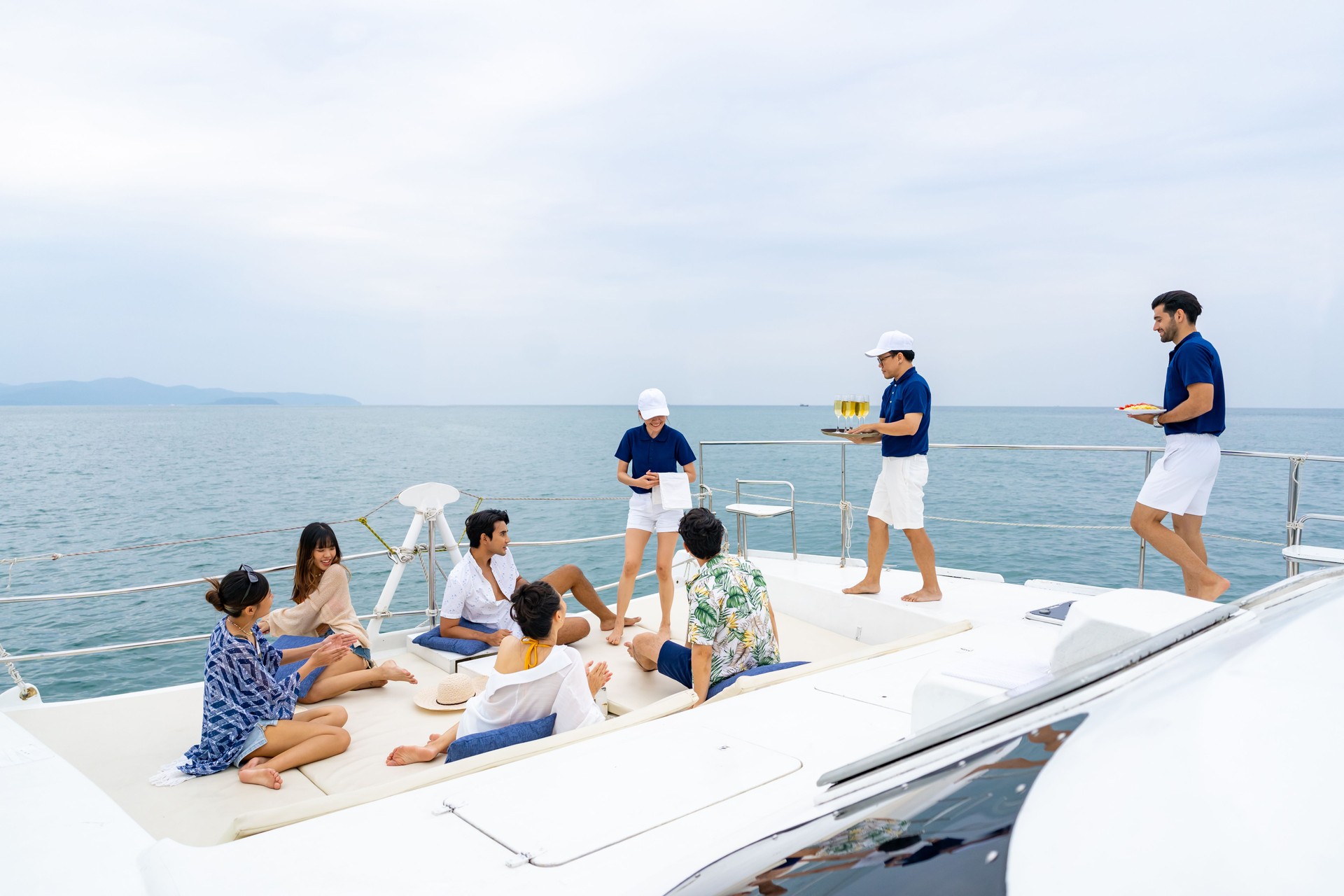 Yacht crew serving food and drink to passenger on luxury catamaran boat sailing in the ocean.